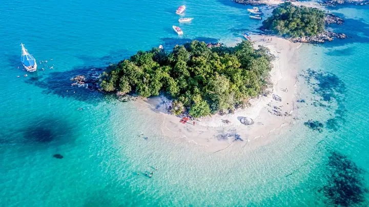 Vista de cima de ilha com banco de areia e água azul-turquesa, com barcos ao redor