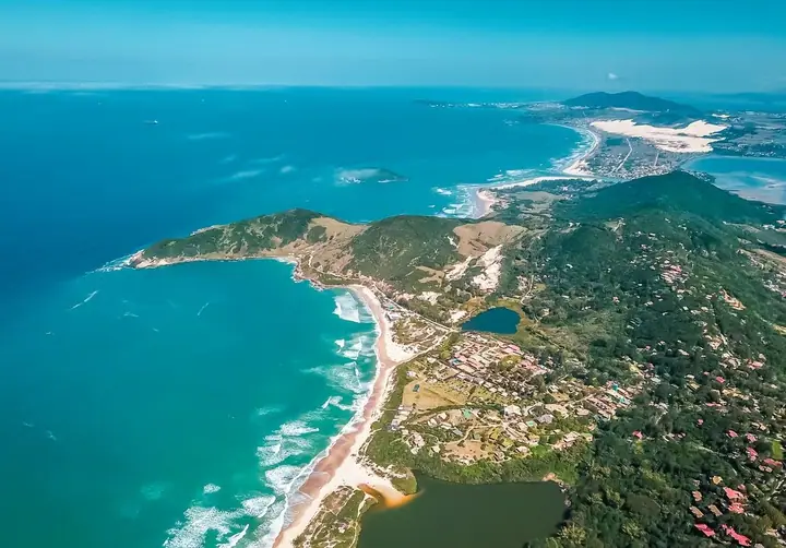 Vista aérea do litoral com lagoa, praias, dunas, morros e vila entre a vegetação