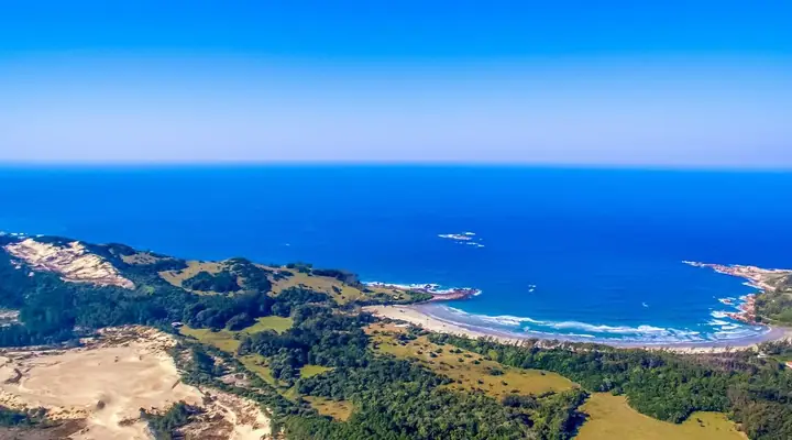 Vista aérea de praia em meia-lua entre dunas, morros e o mar azul