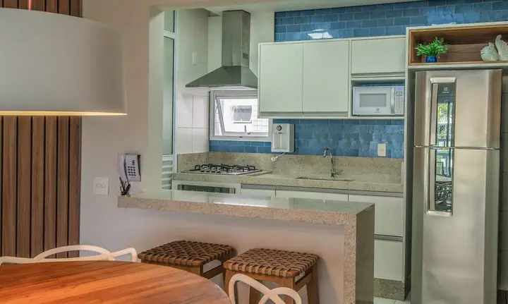 Cozinha americana com bancada de granito, banquetas de fibra e parede de azulejos azuis