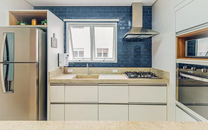Cozinha com azulejos azuis tipo metrô, coifa de inox, geladeira e armários claros