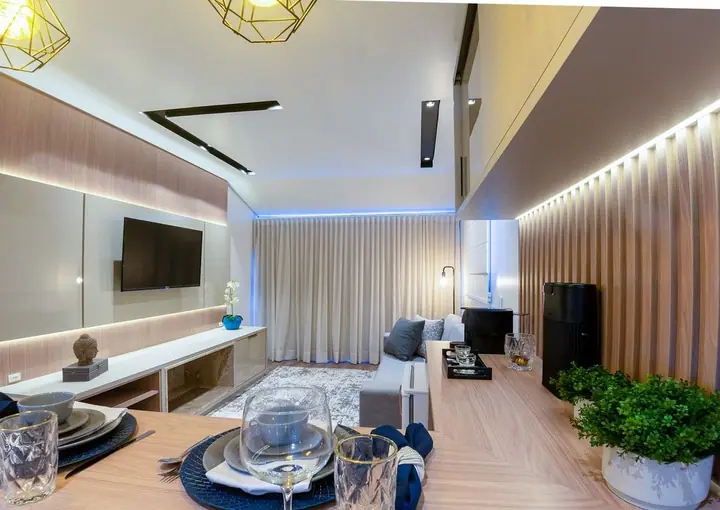 Living de chalé com painel de madeira ripada iluminado por LED, sofá, TV e mesa posta em primeiro plano