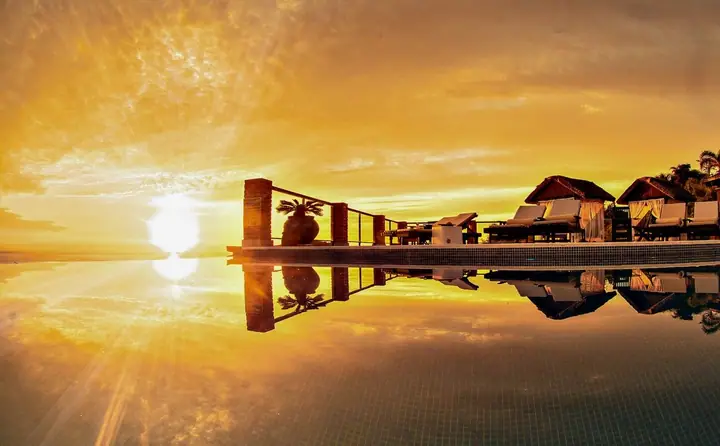 Sol refletido na piscina de borda infinita, com espreguiçadeiras e guarda-corpo em silhueta