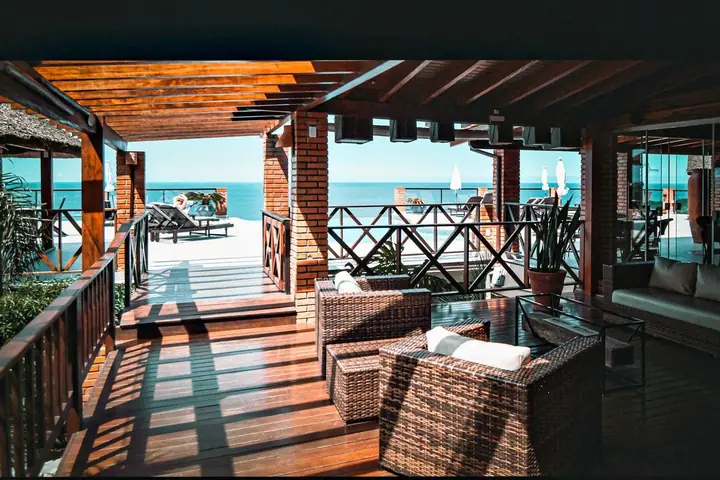 Varanda coberta com pergolado de madeira, poltronas de fibra e deck que se abre para o mar azul